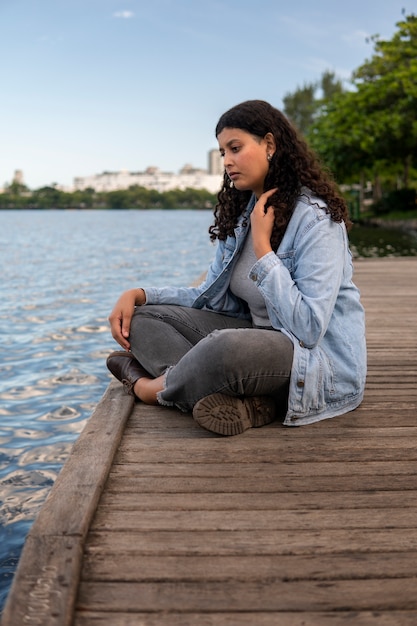 Foto gratuita mujer triste y contemplativa sentada junto al lago