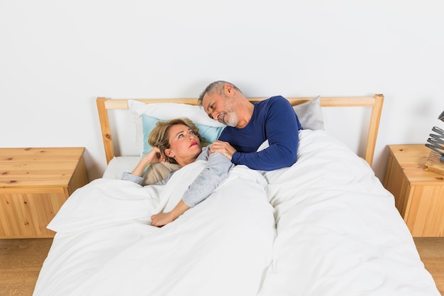 Foto gratuita mujer triste envejecida que miente cerca de hombre en el edredón en cama