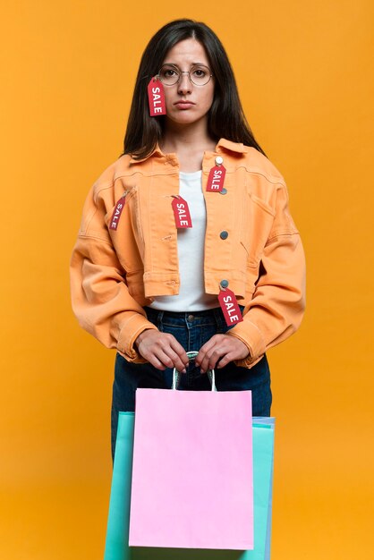 Mujer triste con gafas sosteniendo bolsas de la compra y chaqueta con etiquetas de venta