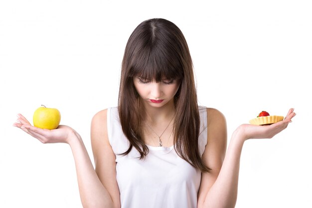 Mujer triste con una manzana en una mano y un pastel en la otra