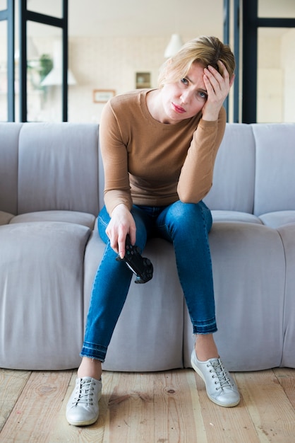 Mujer triste que se sienta con la palanca de mando en el sofá