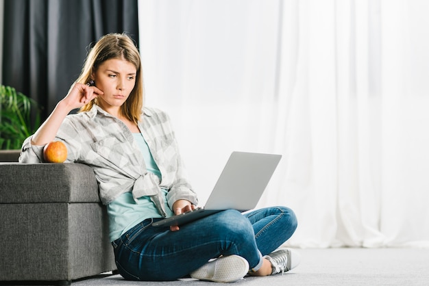 Mujer triste que usa la computadora portátil en piso