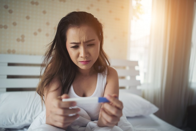 Mujer triste quejándose sosteniendo una prueba de embarazo sentada en la cama
