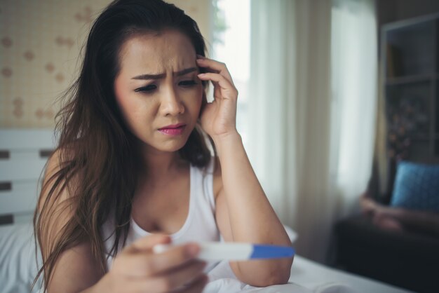 Mujer triste quejándose sosteniendo una prueba de embarazo sentada en la cama