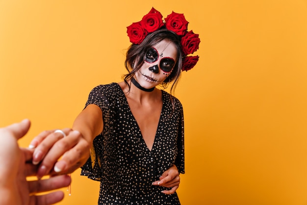 Mujer triste en traje de novia muerta posando en la pared amarilla. Chica latina con escalofriante maquillaje de miedo zombie.