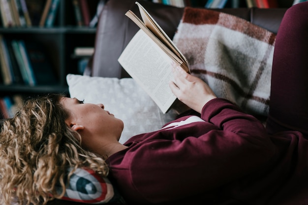 Mujer tumbada en el sofá y leyendo el libro