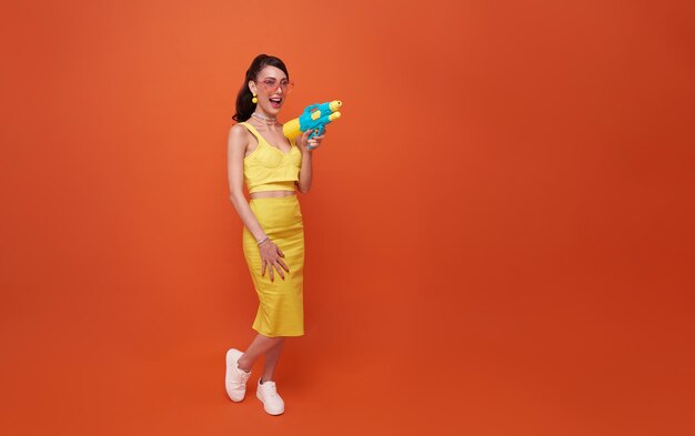 Mujer turista alegre que viaja con pistola de agua durante el festival Songkran con fondo naranja