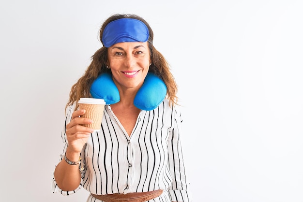 Foto gratuita mujer turista con máscara para dormir con almohada para el cuello bebiendo café sobre un fondo blanco aislado con una cara feliz de pie y sonriendo con una sonrisa segura mostrando los dientes