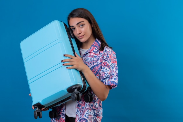 Foto gratuita mujer turista de pie con maleta de viaje con una sonrisa en la cara en azul aislado