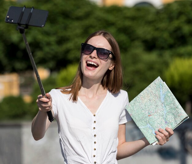 Mujer turística sonriente sosteniendo mapa y tomando selfie