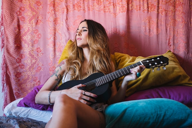 Mujer con ukelele apoyado en almohadas