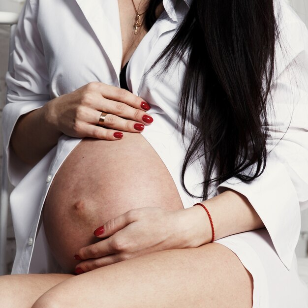 Mujer con uñas rojas sostiene sus manos en el vientre embarazado