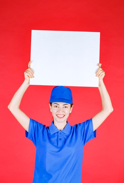 Mujer en uniforme azul y boina sosteniendo un mostrador de información cuadrado blanco y sintiéndose positivo.