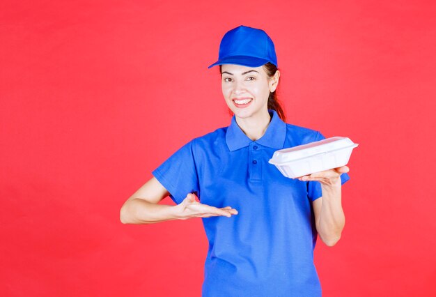 Mujer en uniforme azul sosteniendo una caja de comida para llevar de plástico blanco para la entrega.