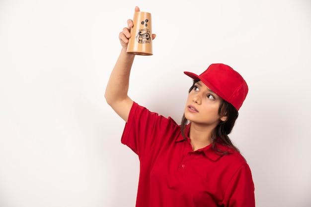 Mujer en uniforme rojo mirando taza vacía sobre fondo blanco.