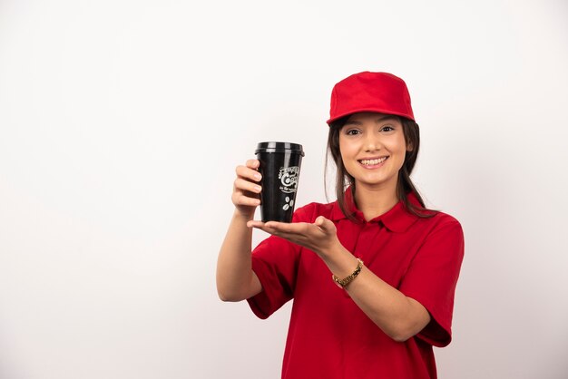 Mujer en uniforme rojo mostrando una taza de café sobre fondo blanco.