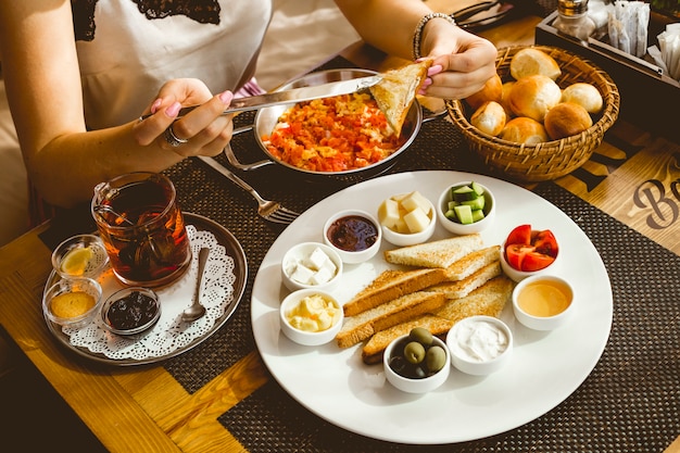 Mujer unta mantequilla sobre tostadas de desayuno set huevo con mantequilla de tomate miel aceitunas queso tomate pepino té mermelada de limón vista lateral