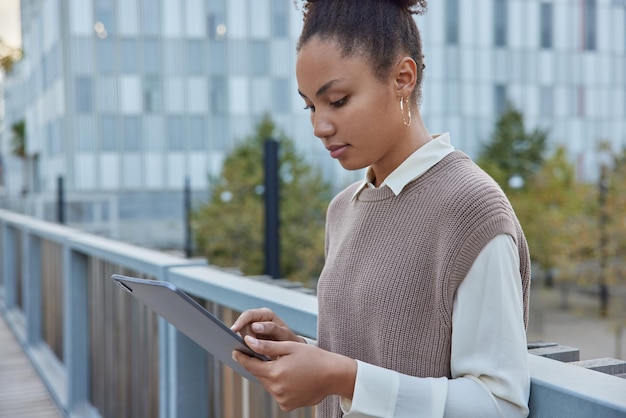 mujer usa tableta en poses de la calle en el puente lee libros en línea o verifica los feeds en las redes sociales a través de wifi concentrado en la pantalla navega por las páginas del sitio web