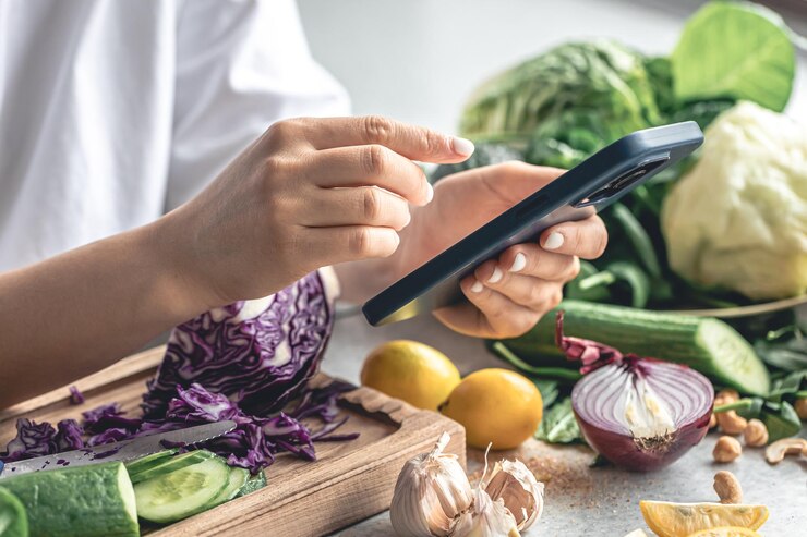 Foto gratuito una mujer usa un teléfono inteligente en la cocina mientras prepara una ensalada de verduras