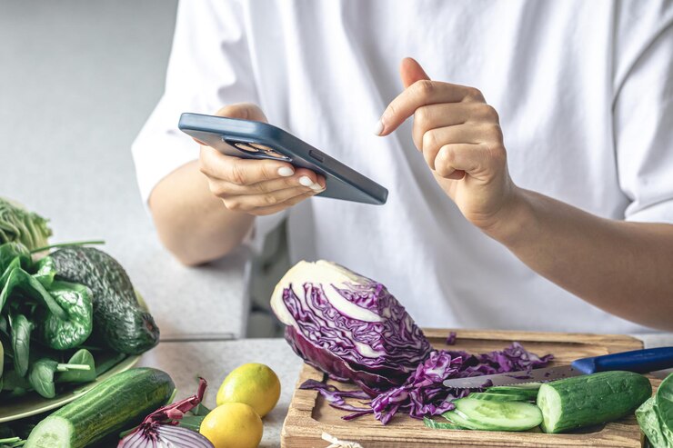 Foto gratuito una mujer usa un teléfono inteligente en la cocina mientras prepara una ensalada de verduras