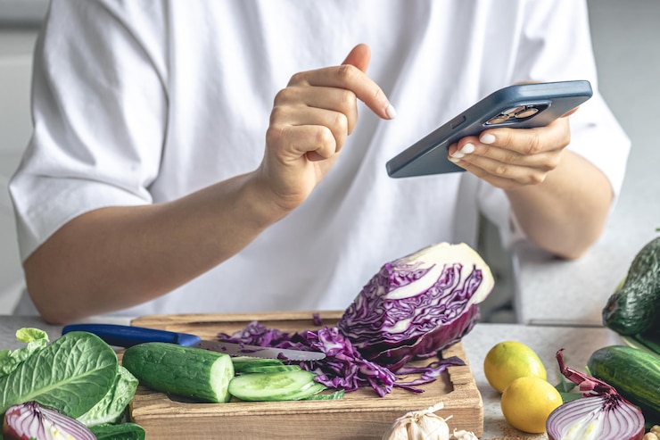 Foto gratuito una mujer usa un teléfono inteligente en la cocina mientras prepara una ensalada de verduras