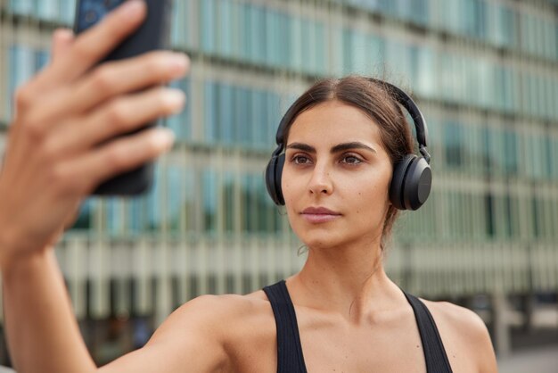 La mujer usa el teléfono para llamadas en línea o se toma una selfie en la cámara frontal durante el entrenamiento físico tiene una expresión segura y pasa tiempo libre en un lugar urbano