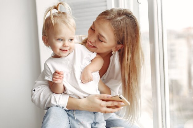 La mujer usa el teléfono. Madre con camisa blanca está jugando con su hija. La familia se divierte los fines de semana.