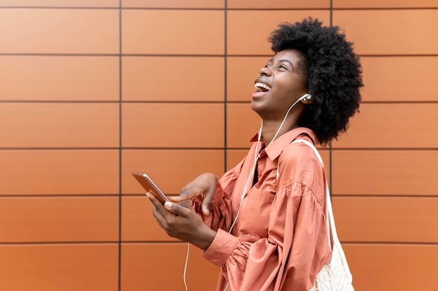 Foto gratuita mujer usando unos auriculares mientras sostiene su teléfono inteligente