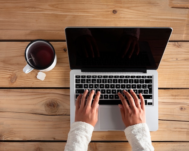 Mujer usando una computadora con té sobre una mesa de madera