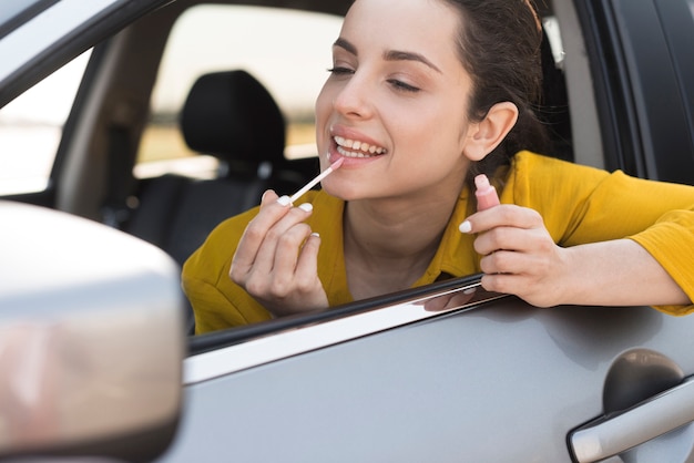 Mujer usando el espejo retrovisor para aplicar lápiz labial