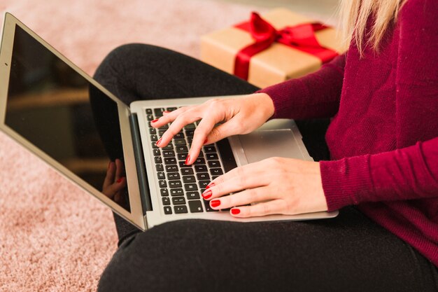 Mujer usando laptop cerca de caja de regalo