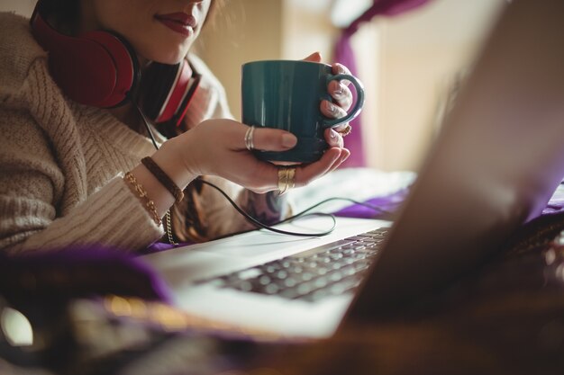 Mujer usando laptop mientras toma café en la cama