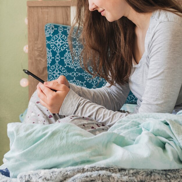 Mujer usando smartphone mientras está en la cama