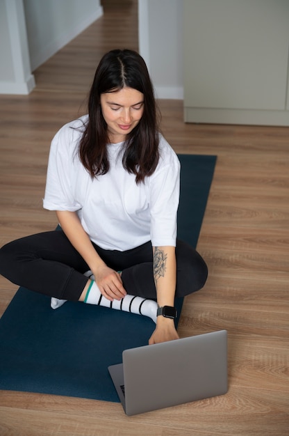 Mujer usando su laptop y haciendo yoga en casa durante la cuarentena