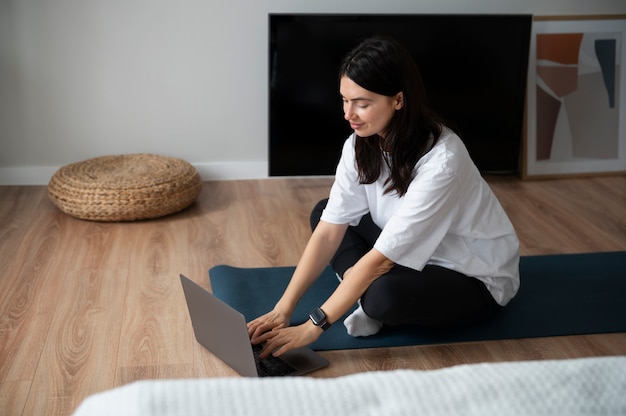 Mujer usando su laptop y haciendo yoga en casa durante la cuarentena