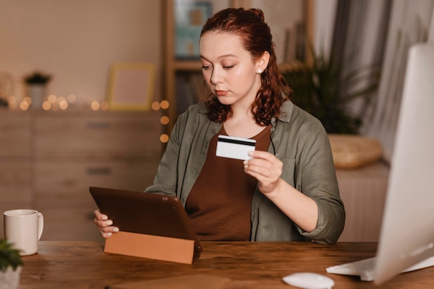 Mujer usando su tableta en casa con tarjeta de crédito