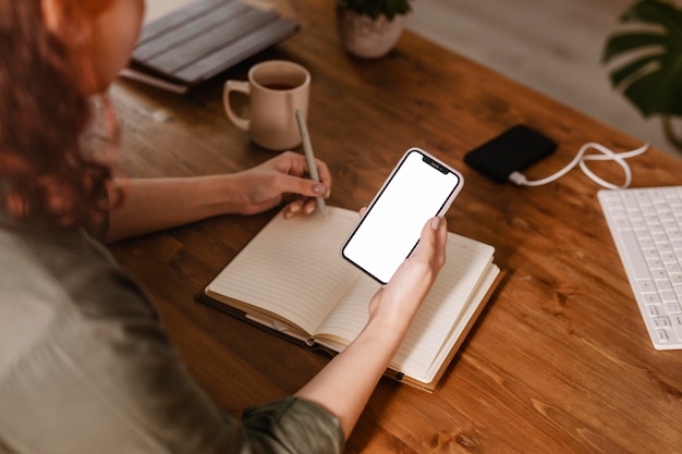 Mujer usando su teléfono inteligente y escribiendo en la agenda