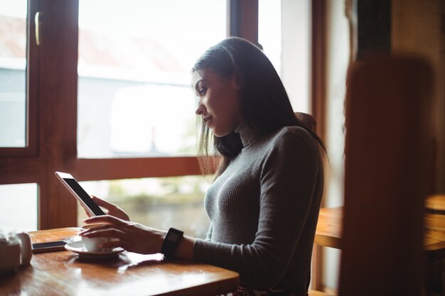 Mujer usando tableta digital mientras toma una taza de café