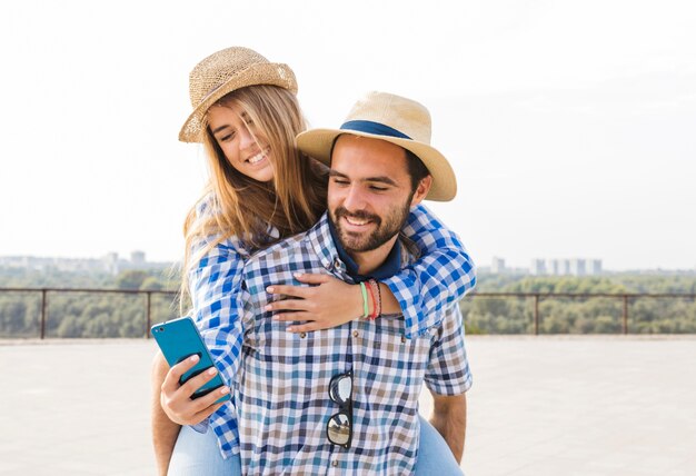 Mujer usando un teléfono celular mientras lleva a cuestas la espalda de su novio