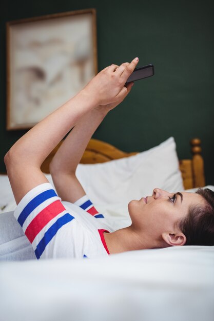 Mujer usando un teléfono móvil mientras está acostado en la cama