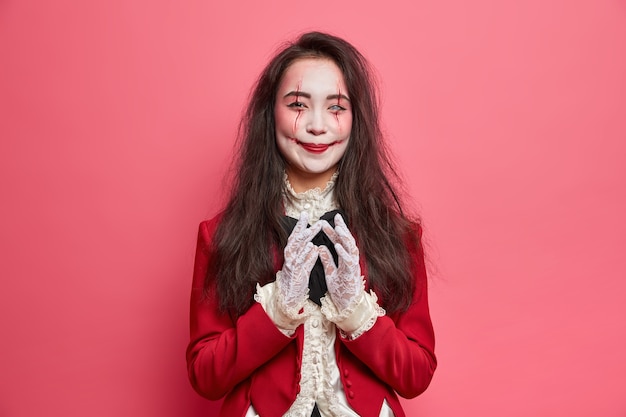 Foto gratuita la mujer vampiro feliz tiene un plan diabólico y la intención de hacer algo usa maquillaje de halloween y poses de disfraces de disfraces en el interior contra la pared rosada