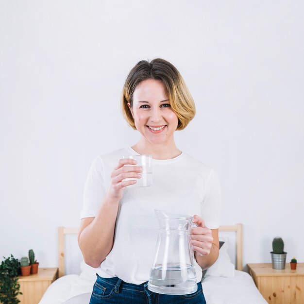 Mujer con vaso y jarra en el dormitorio