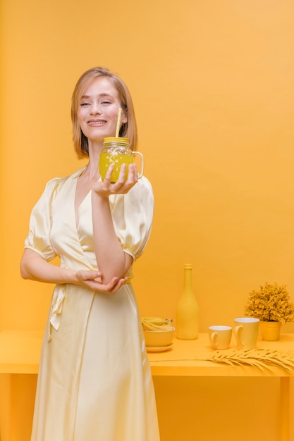 Foto gratuita mujer con vaso de limonada en un escenario amarillo