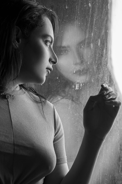 Mujer en la ventana mirando a la lluvia, foto en blanco y negro