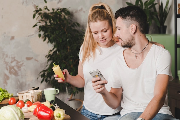 Mujer con verdura en la mano mirando el teléfono celular por su novio