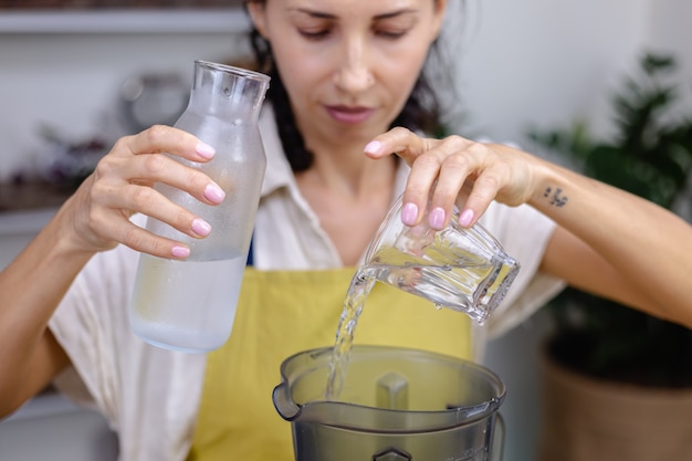 Mujer vertiendo agua en una botella de vidrio y la licuadora en la cocina