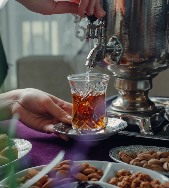 Mujer vertiendo agua caliente en vaso con té negro de samovar