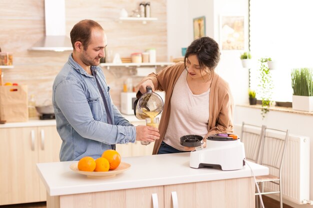 Mujer vertiendo batido nutritivo en vasos para ella y su marido. Estilo de vida saludable, despreocupado y alegre, comiendo dieta y preparando el desayuno en una acogedora mañana soleada