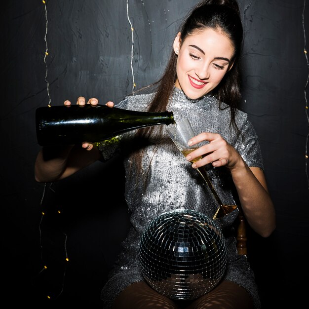 Mujer vertiendo champán en vaso junto a bola de discoteca