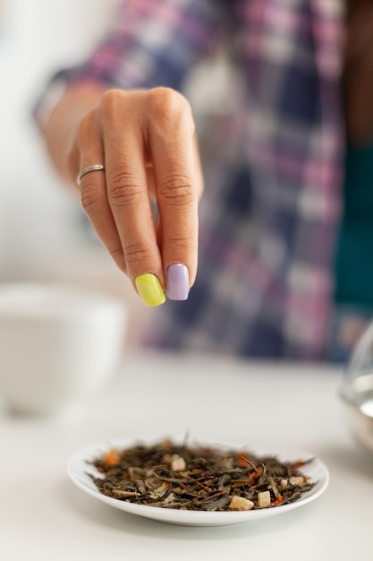 Mujer vertiendo hierbas aromáticas mientras prepara té